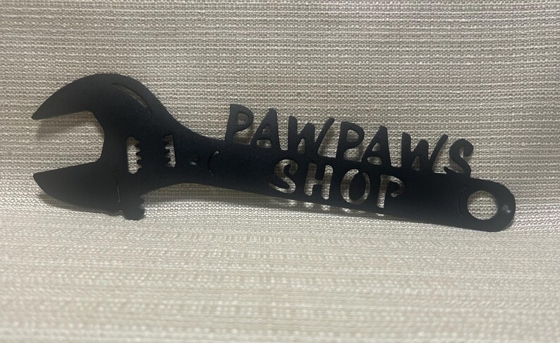 May include: Black metal wrench shaped sign with the words "Paw Paws Shop" cut out.