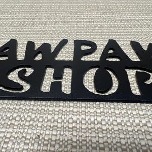May include: Black metal sign with the words "Paw Paw Shop" cut out in a whimsical font.