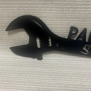 May include: Black metal wrench with the words "Paw Shop" cut out.