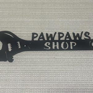 May include: Black metal wrench shaped sign with the text "Paw Paws Shop" cut out.