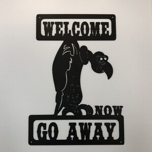 May include: Black metal sign with a cartoon vulture holding a sign that says "Welcome". Below the vulture is another sign that says "Now Go Away".