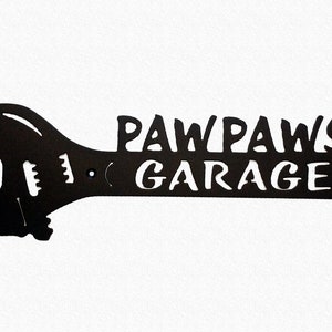 May include: Black metal wrench shaped sign with the text "Paw Paws Garage" in white lettering.