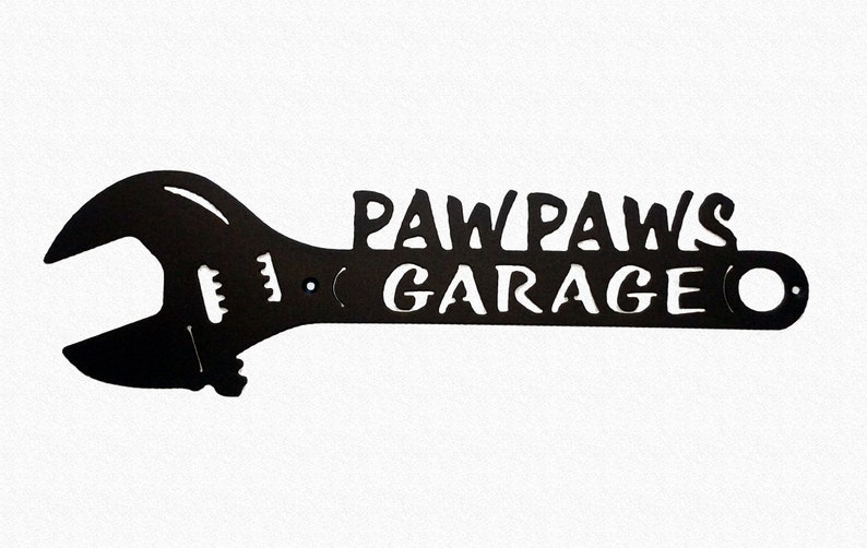 May include: Black metal wrench shaped sign with the text "Paw Paws Garage" in white lettering.