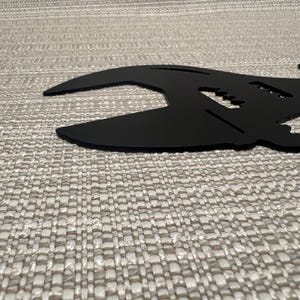 May include: Black metal wrench silhouette wall decor. The wrench is shaped like a guitar with a headstock and strings.