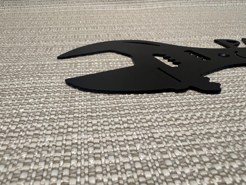 May include: Black metal wrench silhouette wall decor. The wrench is shaped like a guitar with a headstock and strings.