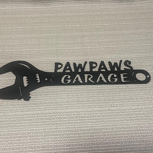 May include: Black metal wrench silhouette with the text "Paw Paws Garage" cut out.