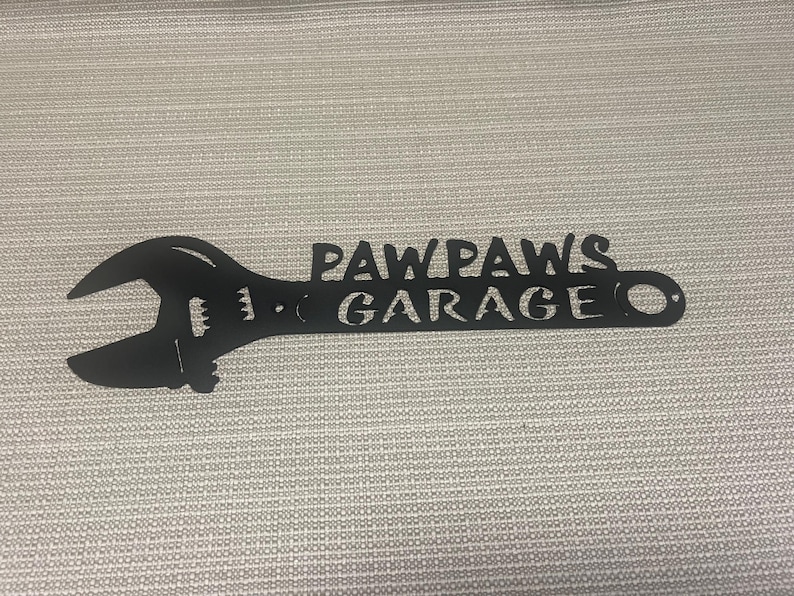 May include: Black metal wrench silhouette with the text "Paw Paws Garage" cut out.