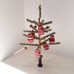 May include: A small artificial Christmas tree decorated with red and white fabric ornaments and small bells. The tree is on a black stand.