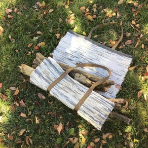 Puede incluir: Dos bolsas de mano hechas a mano de tela tejida, una abierta y otra plegada, con correas marrones. Las bolsas son blancas, grises y beige, y est&aacute;n sobre hierba verde con hojas ca&iacute;das. La bolsa plegada contiene varios trozos de madera.