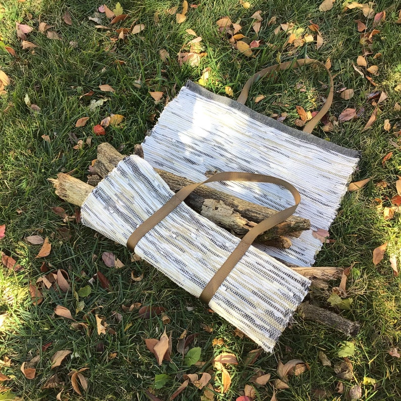 Puede incluir: Dos bolsas de mano hechas a mano de tela tejida, una abierta y otra plegada, con correas marrones. Las bolsas son blancas, grises y beige, y est&aacute;n sobre hierba verde con hojas ca&iacute;das. La bolsa plegada contiene varios trozos de madera.