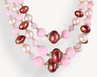 May include: A three-strand necklace with pink and brown beads. The necklace features a mix of round and oval beads, with some beads having a metallic finish.