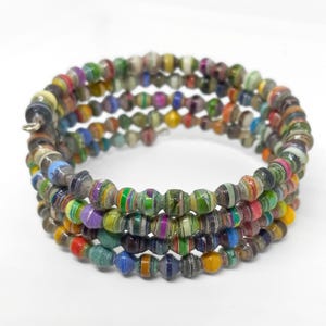 May include: A multi-strand coil bracelet constructed from numerous small, barrel-shaped beads. Each bead features a vibrant, multi-colored pattern with stripes of green, blue, yellow, red, purple, and black, creating a textured, layered appearance.