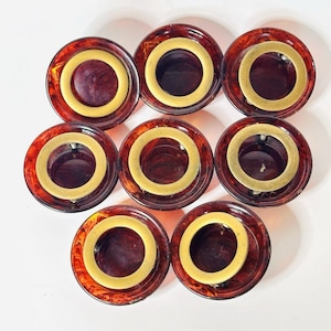 May include: Eight vintage cabinet knobs. Each knob features a dark amber-colored, circular base with a brass-colored ring around a central opening. The knobs are arranged in a circular pattern against a white background.