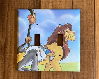May include: A double light switch cover featuring a cartoon image of Simba, Rafiki, and Pumbaa from Disney's The Lion King.
