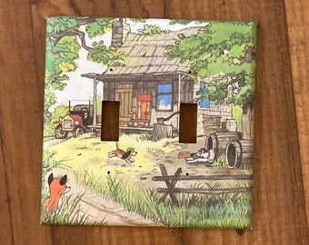 May include: A light switch cover featuring a cartoon illustration of a house in the woods with a red truck, two dogs, and a fox. The switch cover is made of white ceramic with a glossy finish.