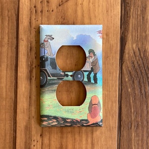 May include: A light brown, rectangular wall plate with a double outlet. The plate features a colorful illustration of a cartoon dog, a man, and a car. The illustration is from the Disney movie The Fox and the Hound.