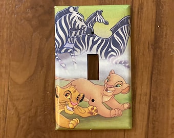 May include: A light switch cover featuring a colorful illustration of zebras and lion cubs from the Disney movie The Lion King. The cover is made of durable plastic and is easy to install.