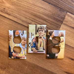 May include: Three light switch covers featuring images of the Golden Girls. The center cover shows a close-up of Bea Arthur, while the left and right covers show the full cast.