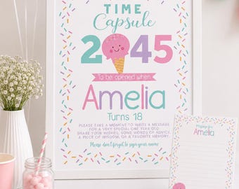 May include: A framed Time Capsule sign with the text "2045" and "Amelia Turns 18". The sign has a colorful ice cream cone graphic and confetti-like sprinkles. A matching note card and pink pen are on the table.
