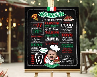 Op de afbeelding: Een zwart schoolbord met een groen en rood Italiaans vlagontwerp. Het bord zegt "Oliver's My 1st Birthday" en somt details op over het eerste jaar van het kind, waaronder lengte, gewicht, eerste woorden, favoriete voedingsmiddelen en activiteiten. De foto van het kind is in een koksmuts en met een snor.