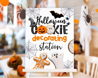 May include: A white rectangular sign on a stand featuring the text Halloween COOKIE decorating station. The design includes illustrations of a black witch hat, a bat, spider webs, a pumpkin cookie, a mummy cookie, a skeleton cookie, and a ghost cookie.