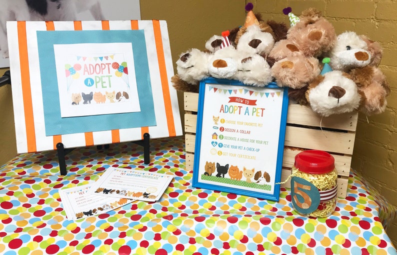 May include: A table with a colorful polka dot tablecloth. There are stuffed animals in a wooden crate, a sign that says "How to Adopt a Pet", and a sign that says "Adopt a Pet".