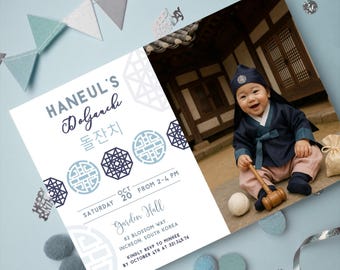 May include: A Doljanchi invitation with a photo of a baby in traditional Korean attire. The invitation features text in English and Korean, with the date, time, and location details. Decorative elements include blue and gray accents.