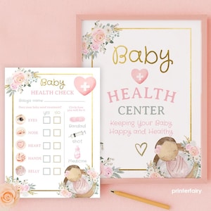 May include: A pink framed sign and a matching health check form. The sign reads "Baby Health Center" with floral accents. The form includes a baby health check with eye, nose, heart, hands, and belly sections.