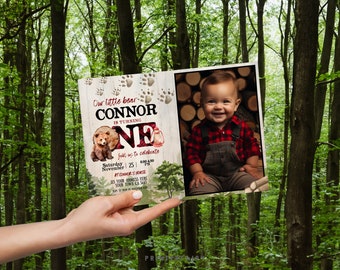 May include: A birthday invitation with a woodland theme. The invitation features the text "Our little bear CONNOR is turning ONE" with a watercolor bear illustration and a photo of a smiling baby. The background is a forest.