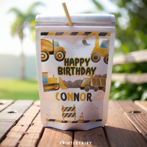 Pode incluir: Uma embalagem de sumo transparente com uma palhinha, com um tema de construção. O design inclui veículos de construção amarelos, o texto "HAPPY BIRTHAY CONNOR" e gráficos de zona de construção. A embalagem está numa superfície de madeira.
