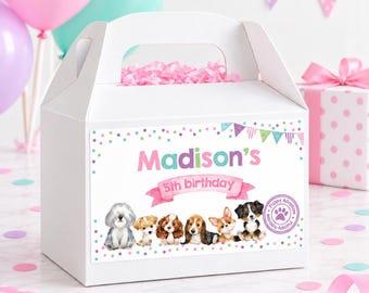 May include: A white cardboard gable box featuring a colorful label with the text Madison's 5th birthday, decorated with illustrations of six different puppies, a purple paw print seal, and a festive bunting banner in pink, green, and purple.