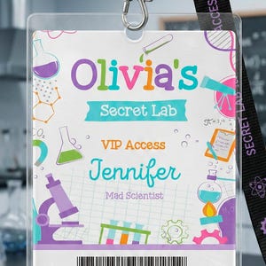 Puede incluir: Una tarjeta de identificación rectangular de plástico en un soporte transparente sujeta a un cordón negro con iconos de engranajes y átomos morados. La tarjeta muestra el texto Olivia's Secret Lab, VIP Access, Jennifer, Mad Scientist, Security Clearance y Level 7 con gráficos científicos.