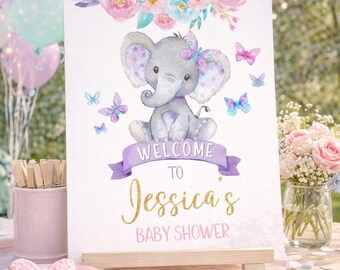 Puede incluir: Un letrero rectangular con una ilustración en acuarela de un elefante gris con una mariposa morada en la cabeza, rodeado de flores y mariposas rosas y azules. El texto dice: WELCOME TO Jessica's BABY SHOWER.