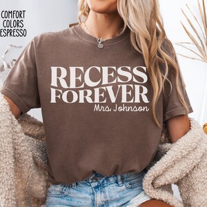 Puede incluir: Camiseta color espresso con las palabras "RECESS FOREVER" en letras blancas grandes. Debajo, "Mrs. Johnson" est&aacute; escrito en una fuente m&aacute;s peque&ntilde;a. La camiseta es parte de la colecci&oacute;n Comfort Colors.
