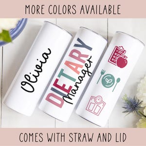 May include: Three white tumblers with different designs. The first tumbler has the name "Olivia" written in black cursive. The second tumbler has the words "Dietary Manager" written in colorful letters. The third tumbler has a red apple, a green plate with a leaf, and a scale with a red arrow. The text "More Colors Available" is at the top of the image and the text "Comes with Straw and Lid" is at the bottom of the image.