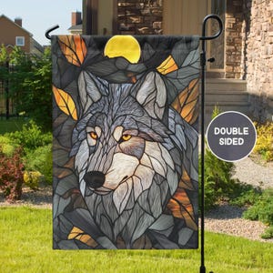 May include: A double-sided garden flag featuring a stained glass style wolf with a yellow moon in the background. The wolf's fur is gray and white, and its eyes are yellow. The flag is surrounded by a dark brown border.