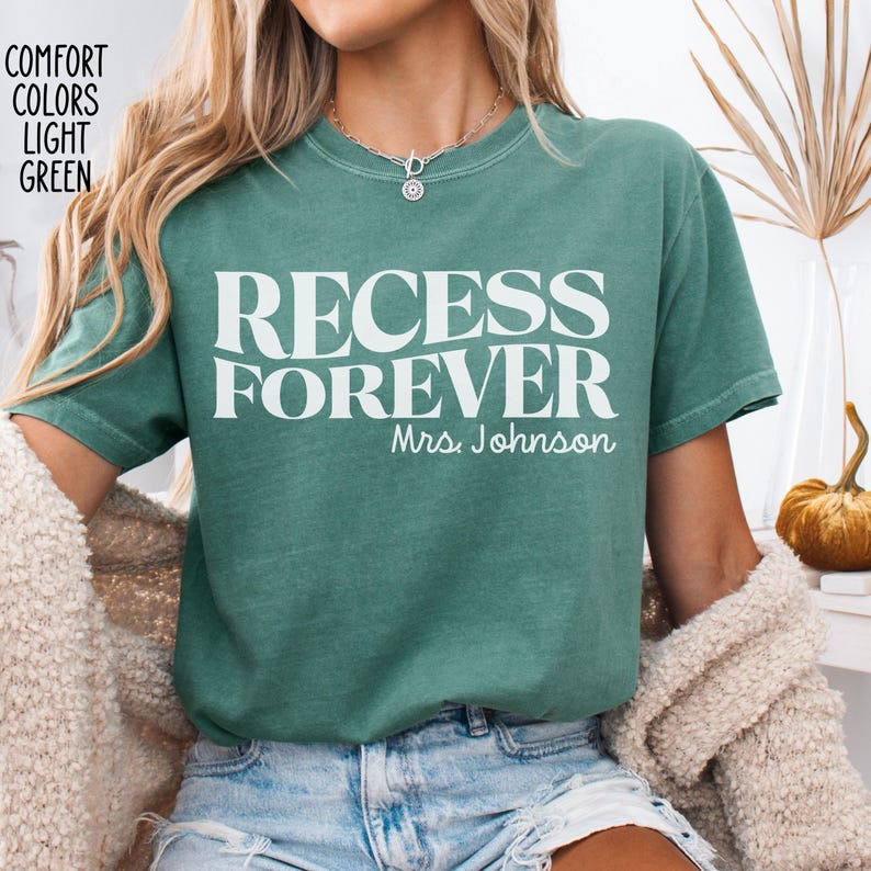 Puede incluir: Camiseta verde claro con las palabras "RECESS FOREVER" en letras blancas grandes. Debajo del texto est&aacute; "Mrs. Johnson" en una fuente m&aacute;s peque&ntilde;a. La camiseta es de estilo comfort colors.