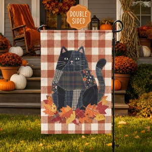 May include: A double-sided garden flag featuring a black cat made of various fabric patterns, including plaid, floral, and houndstooth, sitting on a pile of autumn leaves. The background is a white and orange buffalo check pattern.