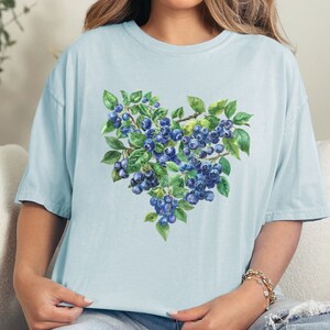 May include: A light blue t-shirt with a watercolor illustration of blueberries in a heart shape.
