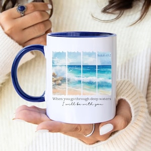 May include: White ceramic mug with a blue interior and handle. The mug features a watercolor painting of a beach scene with ocean waves and the text "When you go through deep waters I will be with you" and "Isaiah 43:2".
