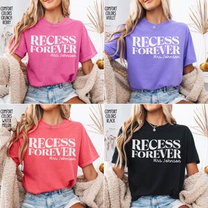 Puede incluir: Cuatro camisetas de diferentes colores: rosa, morado, coral y negro. Cada camiseta tiene la frase "RECESS FOREVER" en letras blancas, con "Mrs. Johnson" debajo. Las camisetas son de manga corta y casuales.