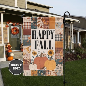 May include: A double-sided garden flag with a patchwork design and the words "HAPPY FALL" in black. The flag features pumpkins, sunflowers, and fall foliage in shades of orange, yellow, and brown. The flag is displayed on a black metal stand in front of a house.