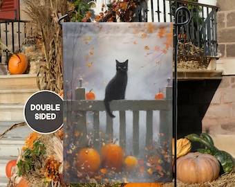 May include: Double-sided garden flag featuring a black cat perched on a fence, with pumpkins and autumn foliage. The artwork has a soft, painterly style, evoking a fall harvest theme. The flag is displayed outdoors, with a house and fall decorations in the background.
