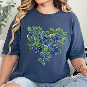 May include: A navy blue t-shirt with a watercolor illustration of blueberries on a branch in the shape of a heart.