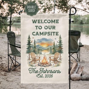 May include: Double-sided garden flag with the text "WELCOME TO OUR CAMPSITE." The flag features a watercolor illustration of a campfire, Adirondack chairs, trees, and a lake. The family name "The Johnsons" and the year "Est. 2026" are also displayed.