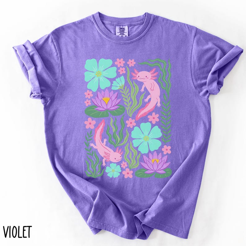 May include: Violet-colored t-shirt featuring a colorful graphic of two axolotls, flowers, and aquatic plants. The design includes pink axolotls, teal and pink flowers, and green foliage. The word "VIOLET" is printed at the bottom left.