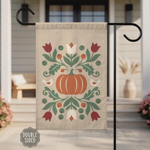 May include: A rectangular garden flag with a beige background featuring a central orange pumpkin surrounded by symmetrical green foliage, red berries, white and red tulips, and two small white birds. The text "DOUBLE SIDED" appears in a badge.