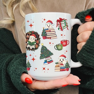 May include: White ceramic mug with a Christmas-themed design featuring a ghost reading a book, a Christmas tree, and stacks of books. The mug has a red handle and a red and white design.