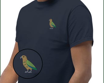 May include: Navy blue t-shirt featuring an embroidered bird design on the chest. The bird has a tan head, green wings, and a blue tail. The t-shirt is made of a soft material and has a classic crew neck.