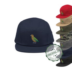 May include: A navy blue five-panel cap with an embroidered parrot design. The parrot is yellow, green, and blue. Additional caps in red, tan, olive green, camouflage, gray, navy, and black are also shown.